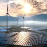 Turbiny wiatrowe nad farmą fotowoltaiczną w mglistym świetle słońca - ograniczenia produkcji OZE we wrześniu 2026